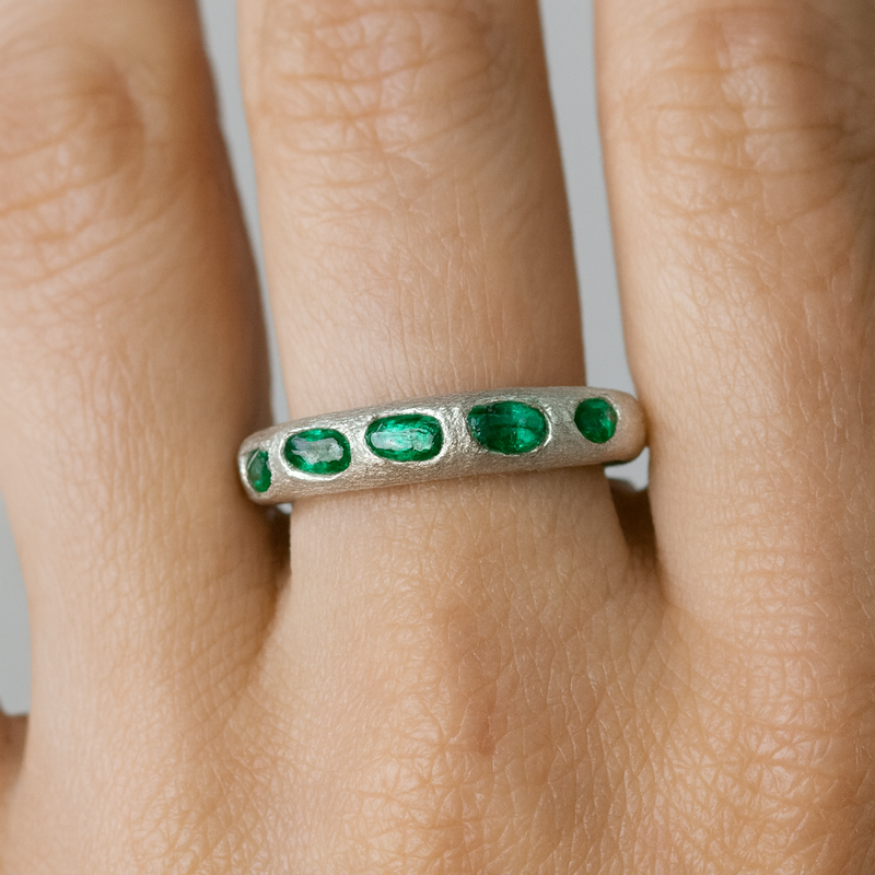 Silver ring with green gemstones on a finger against a neutral background