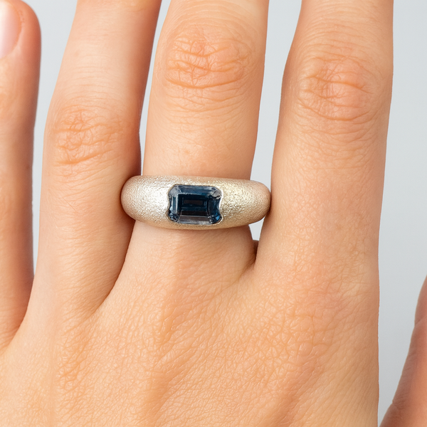 Silver ring with a blue gemstone on a person's finger against a neutral background