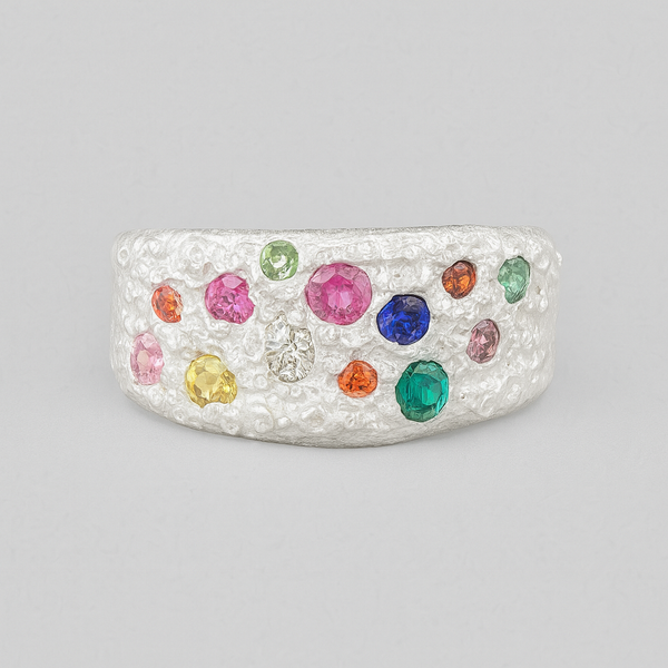Silver ring with multicolored gemstones on a gray background