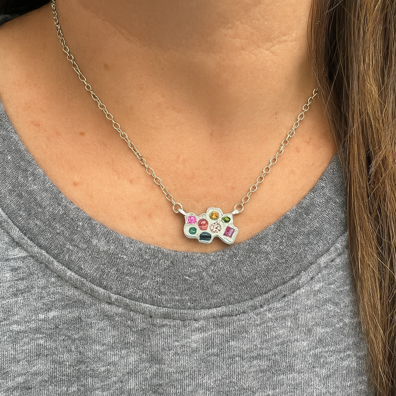 Necklace with a paw-shaped pendant featuring colorful stones worn by a person in a gray shirt.