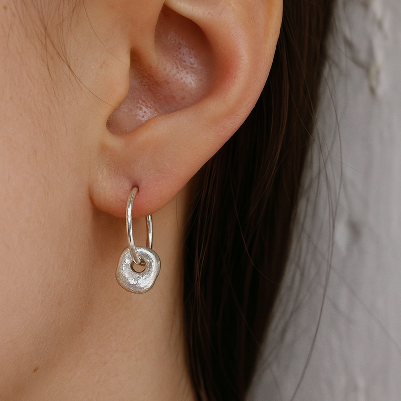 Close-up of an ear wearing a silver hoop earring with a plain background