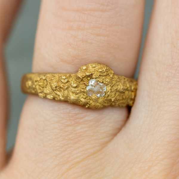 Gold ring with a diamond on a finger against a neutral background