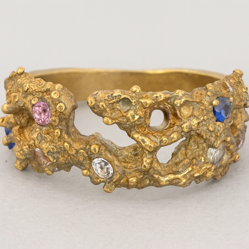 Gold ring with textured design and embedded gemstones on a light gray background