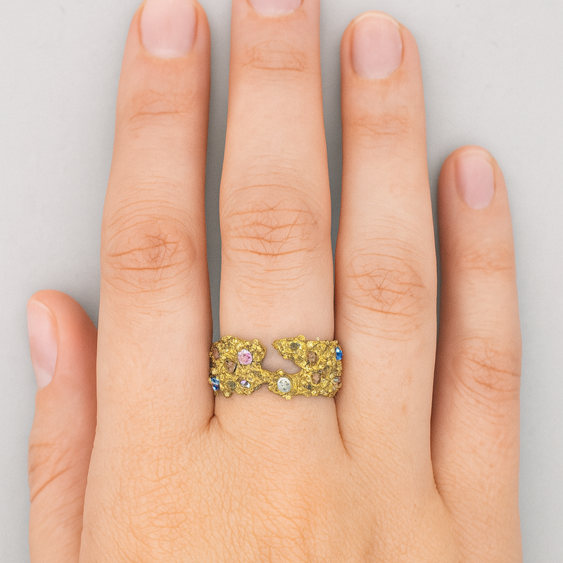 Hand wearing a ring with colorful gemstones on a neutral background