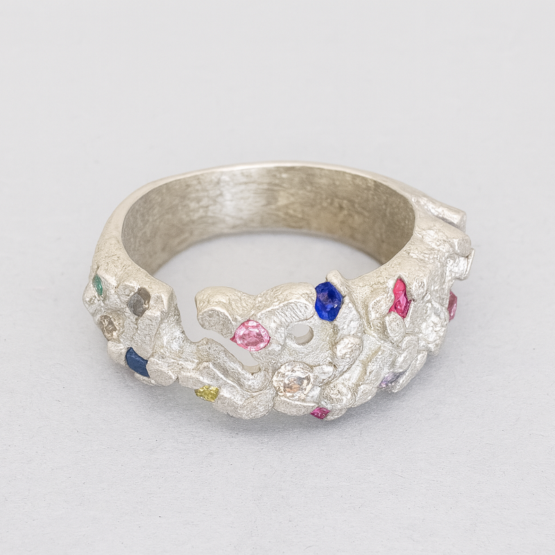Silver ring with colorful gemstones on a light gray background