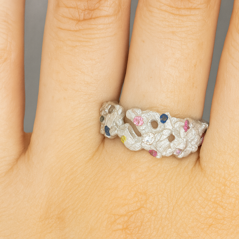 Silver ring with colorful gemstones on a hand against a neutral background