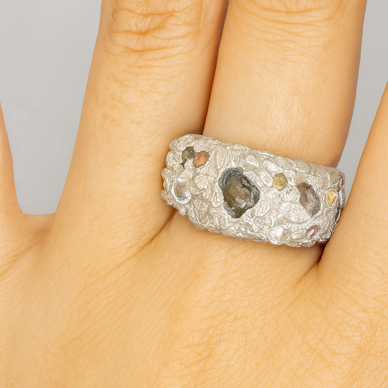 Silver ring with embedded stones on a finger against a neutral background