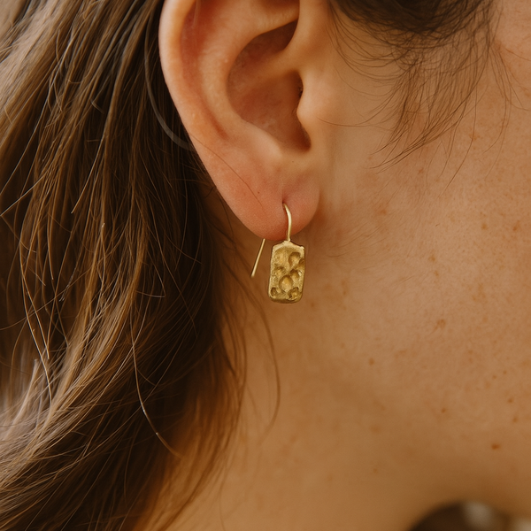 Close-up of an ear wearing a gold earring with a blurred background