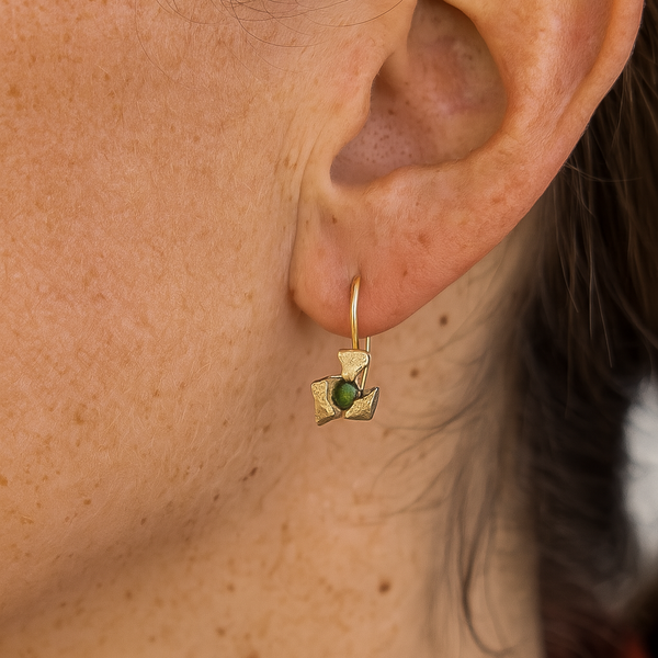 Close-up of an ear wearing a gold earring with a green gemstone.