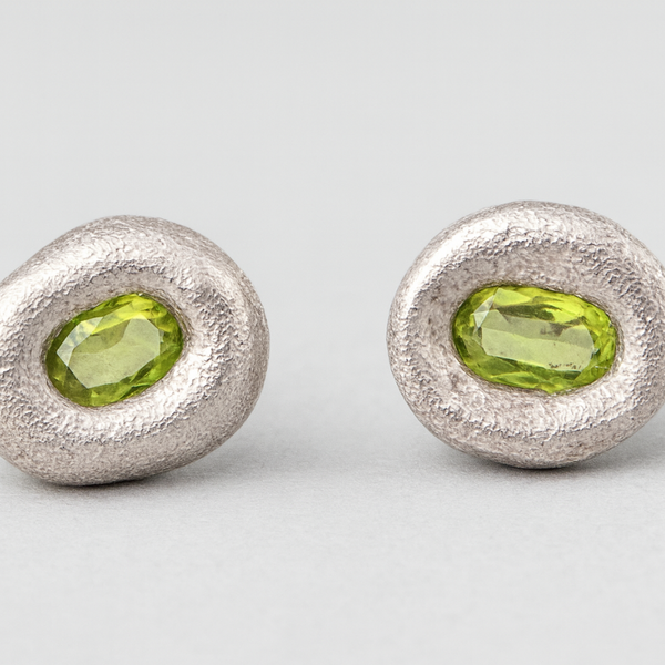 Pair of silver earrings with green gemstones on a light gray background
