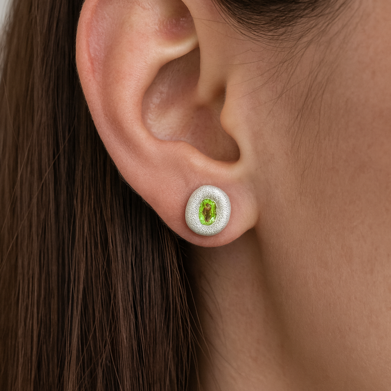 Close-up of an ear wearing a stud earring with a green gemstone.