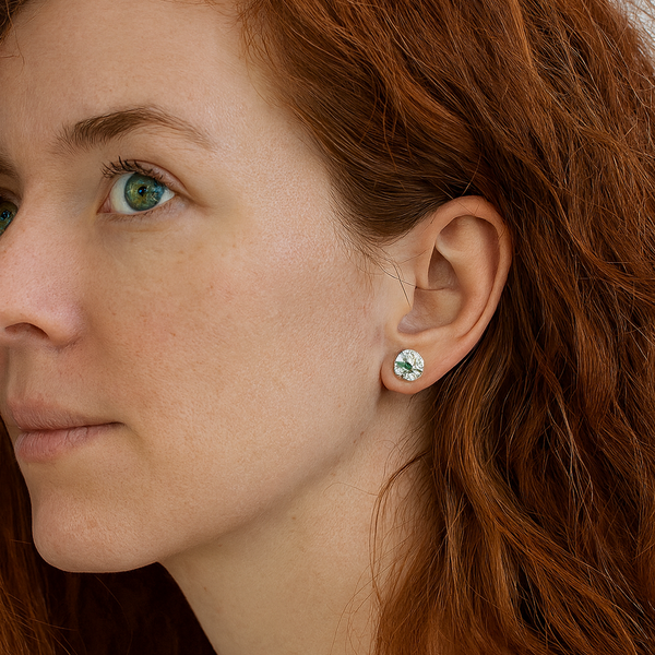 Close-up of a woman with red hair wearing a silver earring with a green gemstone.