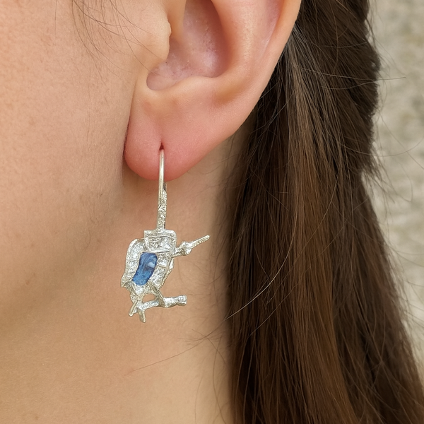Close-up of an ear wearing a diamond earring with a blue gemstone.