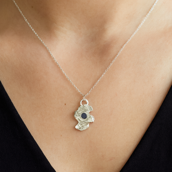 Silver necklace with a pendant featuring a blue gemstone on a person wearing a black top.