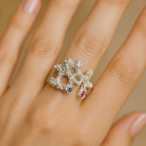 Close-up of a hand wearing a decorative ring with gemstones on a neutral background