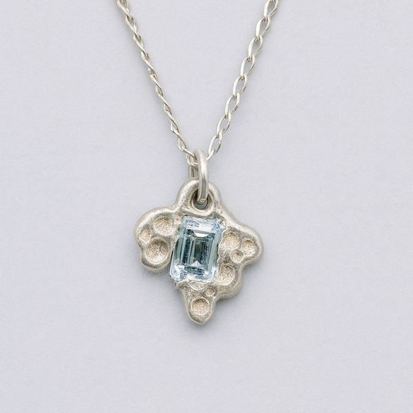 Silver necklace with a pendant featuring a blue gemstone on a light gray background