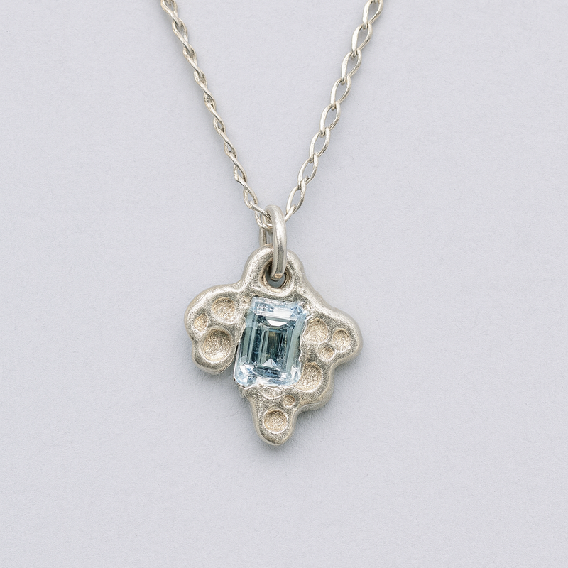 Silver necklace with a pendant featuring a blue gemstone on a light gray background