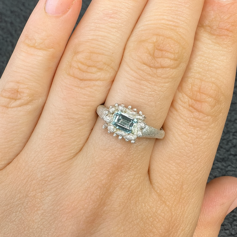 Silver ring with a green gemstone on a hand against a dark background