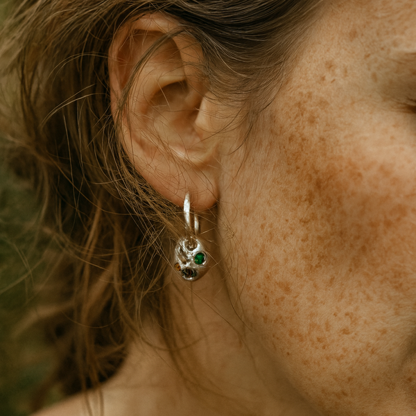 Close-up of a person wearing a silver earring with green stones.