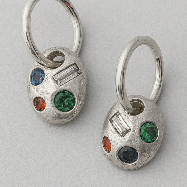 Pair of silver earrings with multicolored gemstones on a light gray background