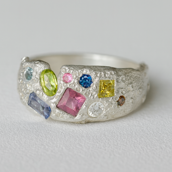 Silver ring with multicolored gemstones on a light gray background