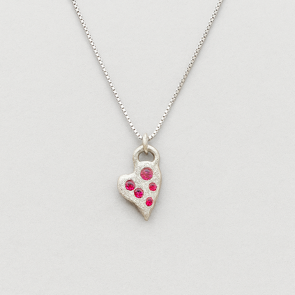 Silver heart-shaped pendant necklace with red stones on a light gray background