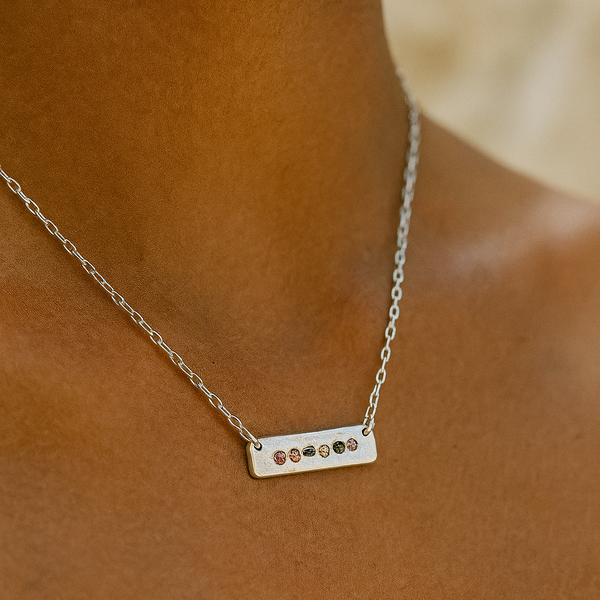 Silver necklace with small stones on a person's neck against a brown background