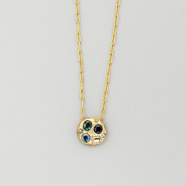 Gold necklace with a pendant featuring three colored stones on a gray background