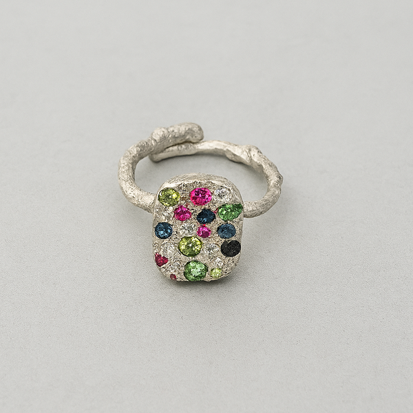 Silver ring with multicolored gemstones on a light gray background