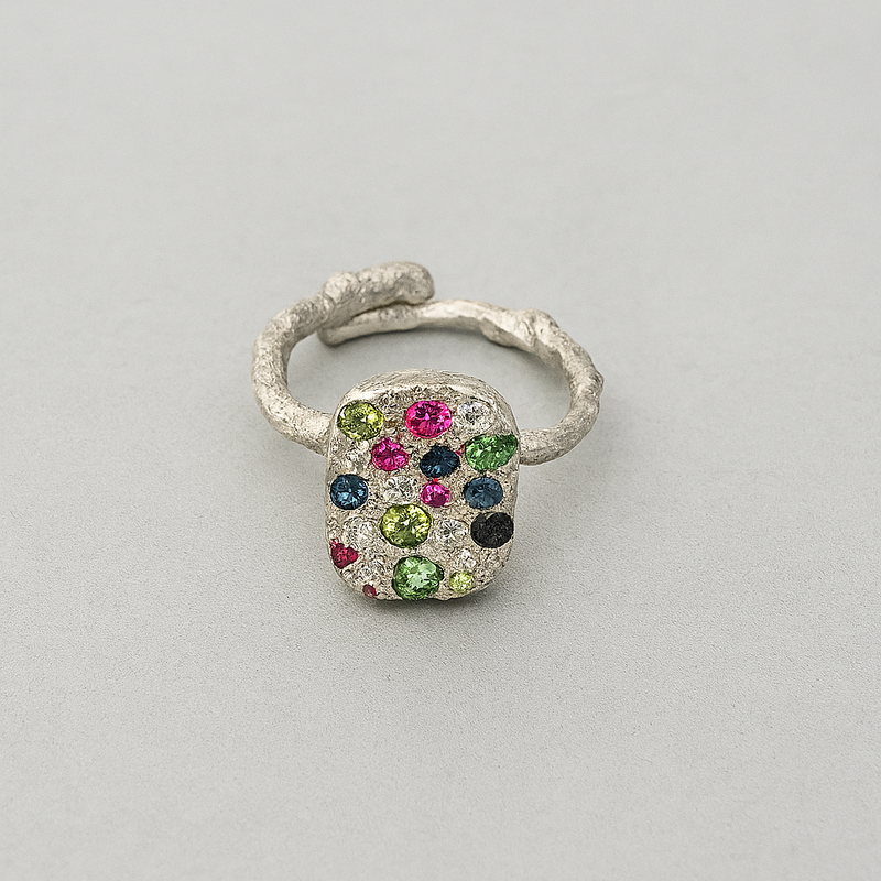 Silver ring with multicolored gemstones on a light gray background