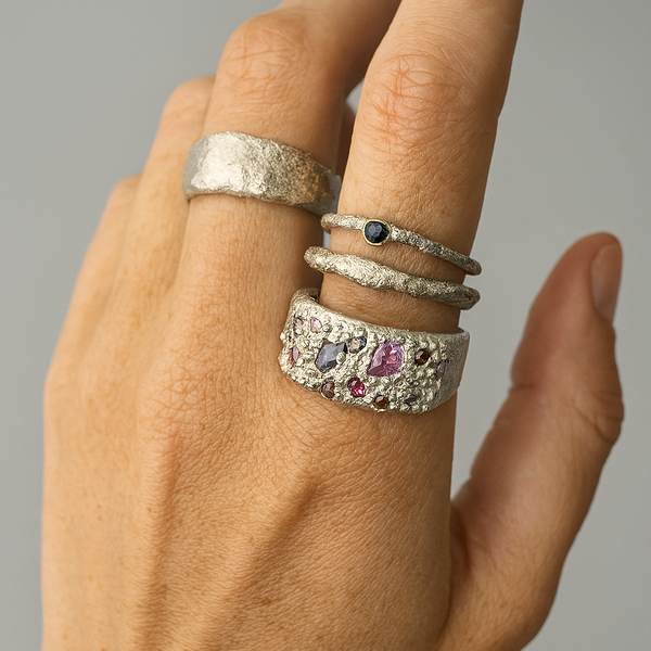Hand wearing multiple silver rings with gemstones on a neutral background