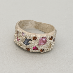 Silver ring with embedded colorful gemstones on a light gray background