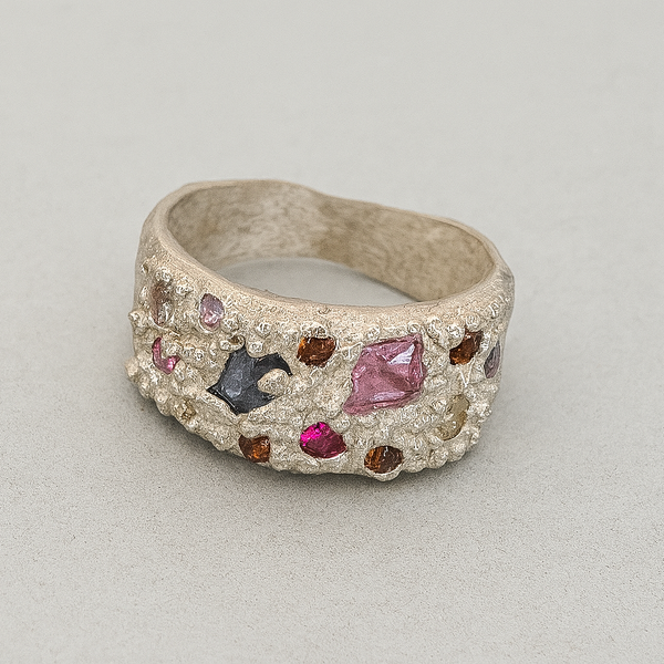Silver ring with embedded colorful gemstones on a light gray background