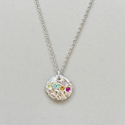 Silver necklace with a round pendant featuring colorful gemstones on a light gray background