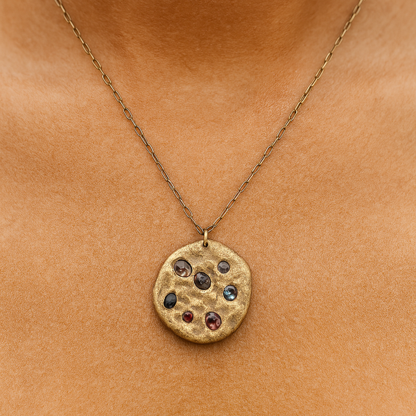 Gold necklace with a round pendant featuring embedded stones on a person's neck.