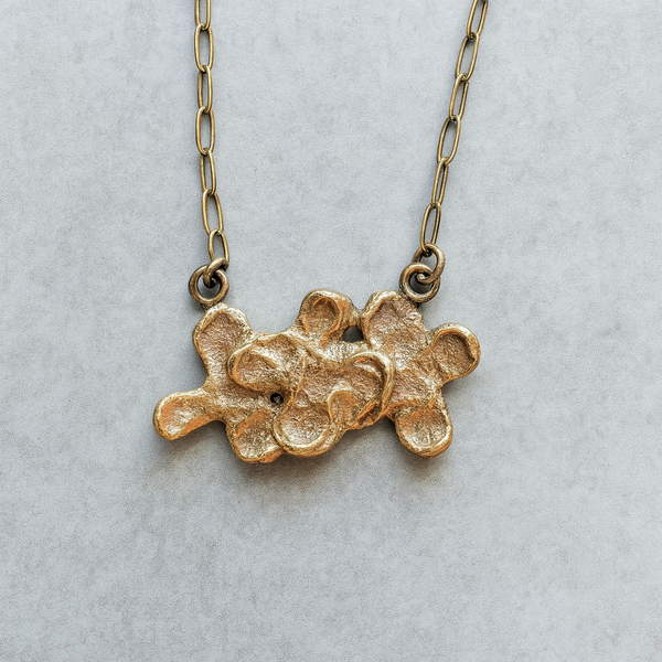 Gold necklace with a textured pendant on a light gray background
