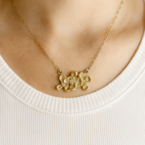Gold necklace with a floral pendant on a person wearing a white shirt.