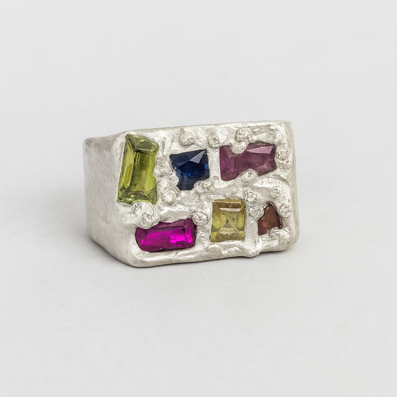 Silver ring with multicolored gemstones on a light gray background