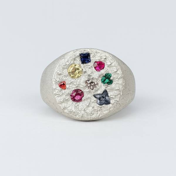 Silver ring with multicolored gemstones on a light gray background