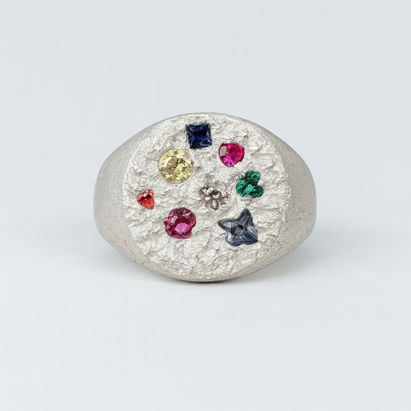 Silver ring with multicolored gemstones on a light gray background