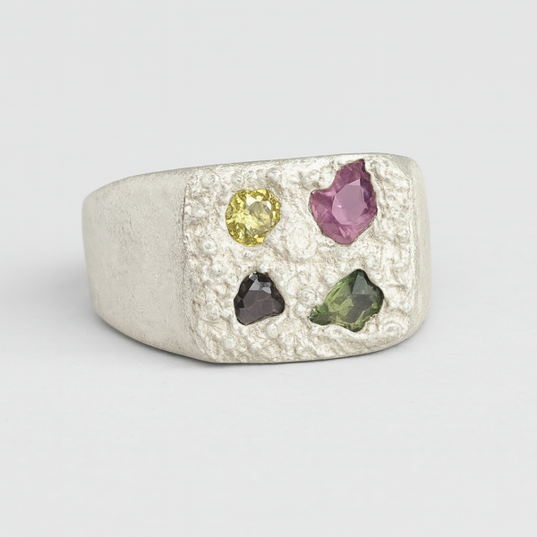 Silver ring with multicolored gemstones on a light gray background