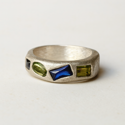 Silver ring with embedded green and blue stones on a light gray background