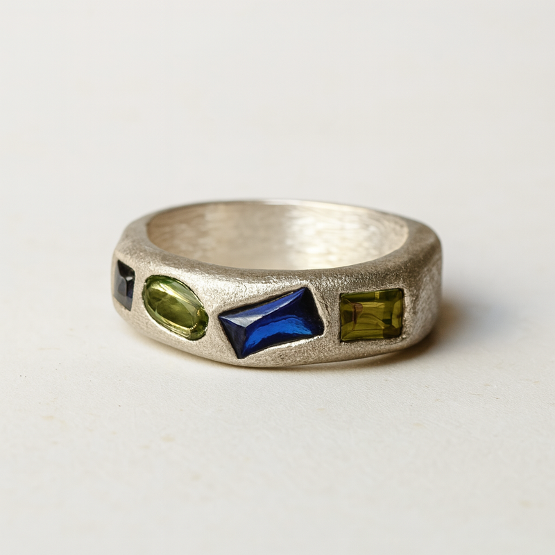 Silver ring with embedded green and blue stones on a light gray background