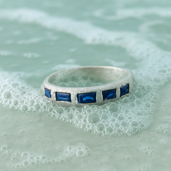 Silver ring with blue gemstones on a textured green surface