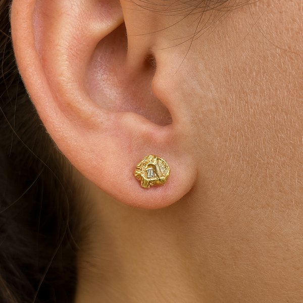 Close-up of an ear wearing a gold earring with a green gemstone.