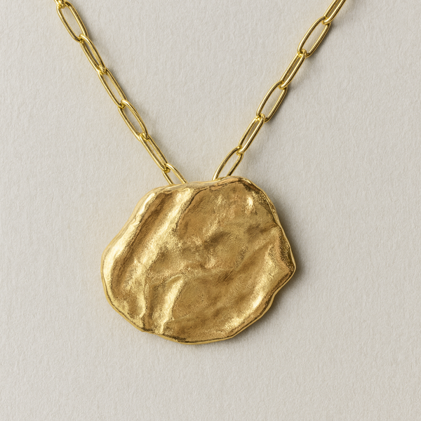Gold necklace with a textured pendant on a light background