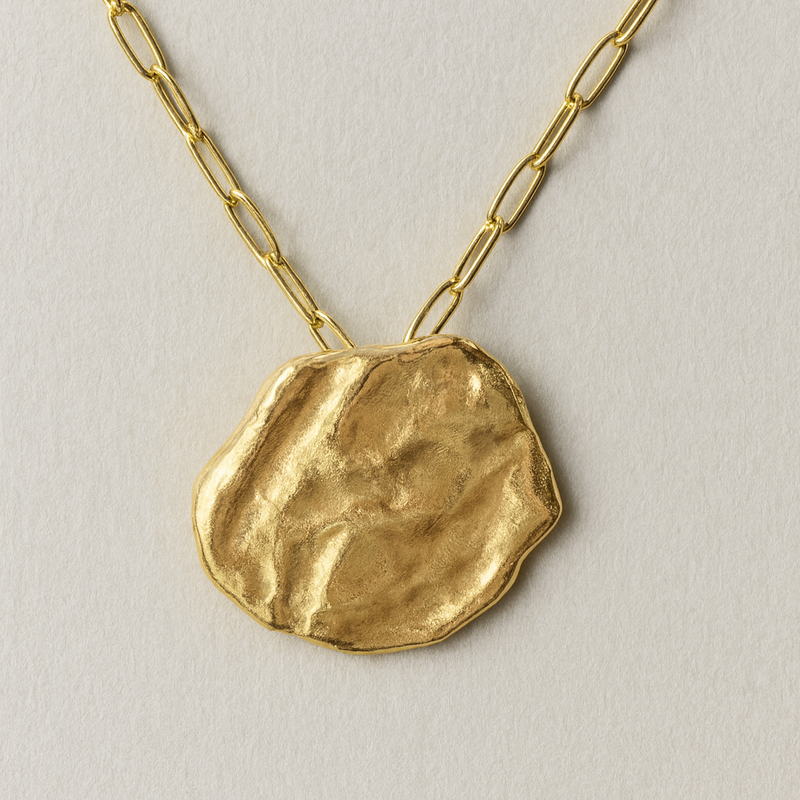Gold necklace with a textured pendant on a light background